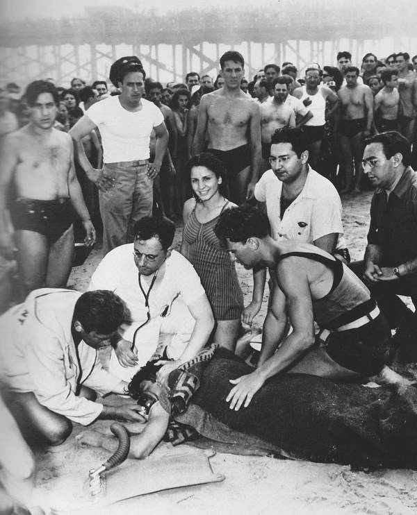 1940. Coney Island. Egy fiatal hölgy nem éppen a legjobb időpontot választotta a mosolyra. Orvosok épp egy fuldoklót próbálnak éleszteni..jpg